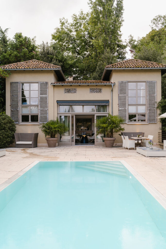 A modern house with large windows and a swimming pool in front, surrounded by trees and patio furniture – an ideal setting for a luxurious wedding in a special location or an exclusive event.